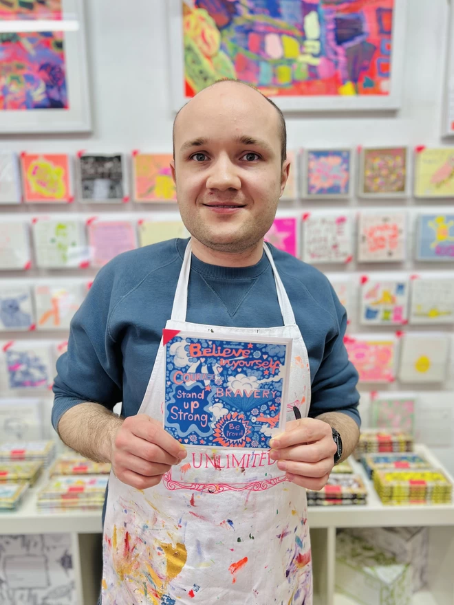 Artist holding a riso printed card called Believe In Yourself with positive affirmations in bright colours