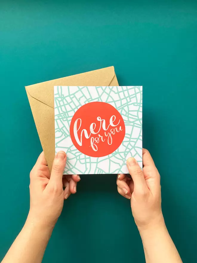 Square 'Here for you' card and brown envelope, held in two hands