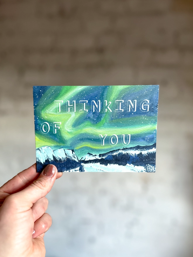 a greetings card featuring an illustration of the northern lights landscape with the text “thinking of you”