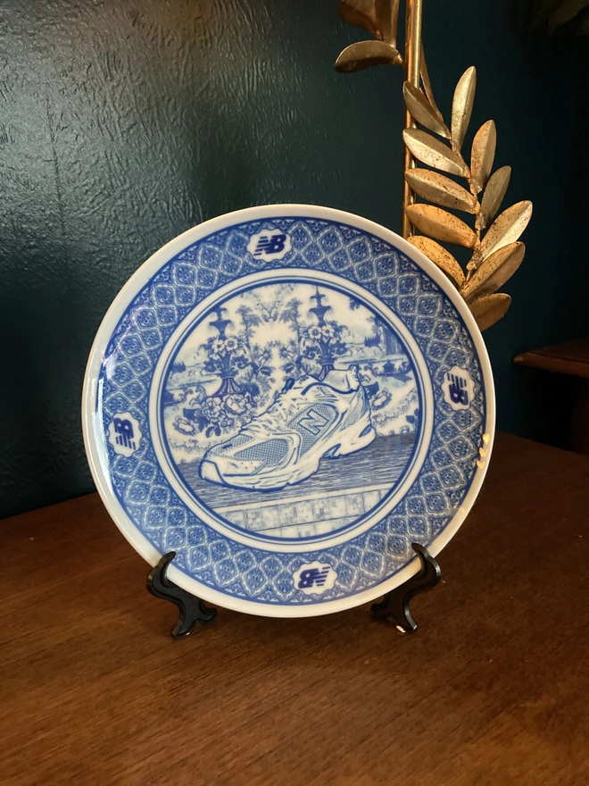 detail of plate showing the New Balance logo. The plate is blue and white in a Delft style featuring an illustration of a New Balance trainer in the centre