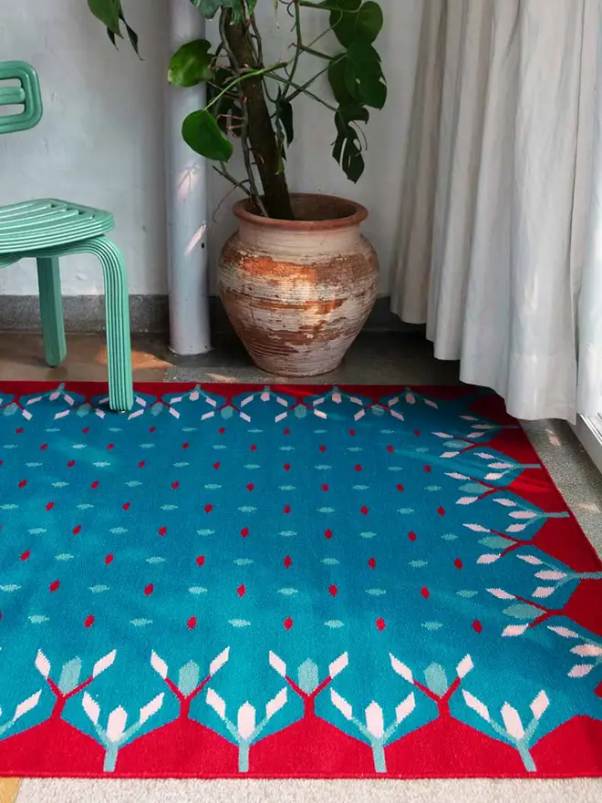 Hedgerow Flatweave Rug, a colourful rug sitting in a decorated room. It is accompanied by some household items.