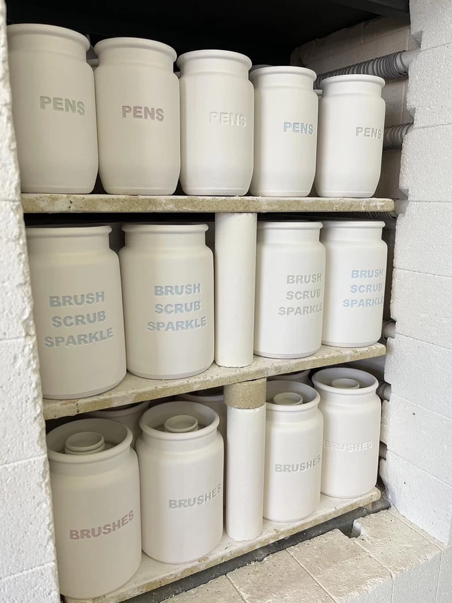 The kiln door is open showing shelves stack with freshly bisque fired ‘Brush Scrub Sparkle’ pots.