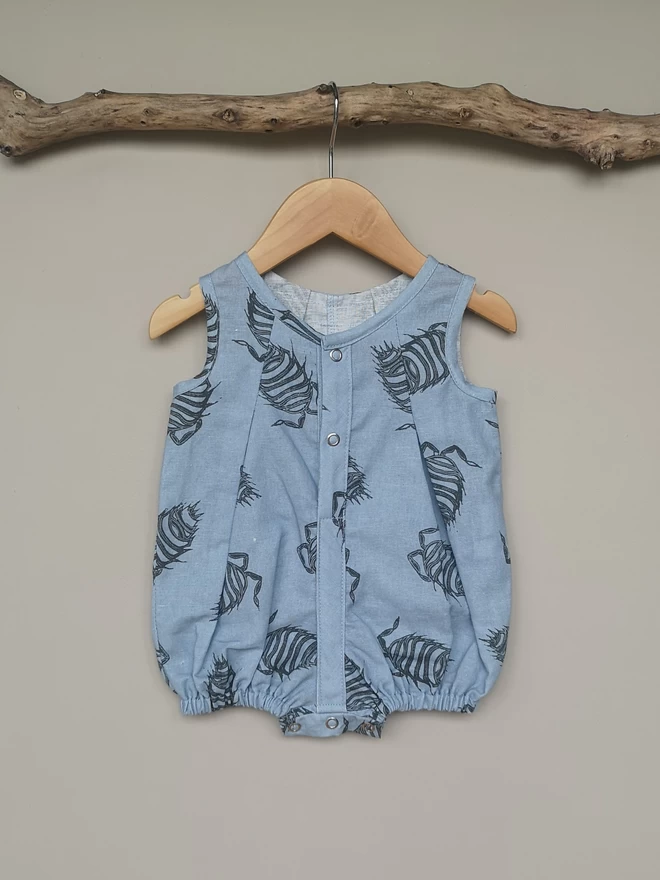 Baby blue cotton linen baby romper. Printed with a charcoal dragonfly. Partially opening centre front and crotch to allow for changing. Sleeveless with a high short leg.