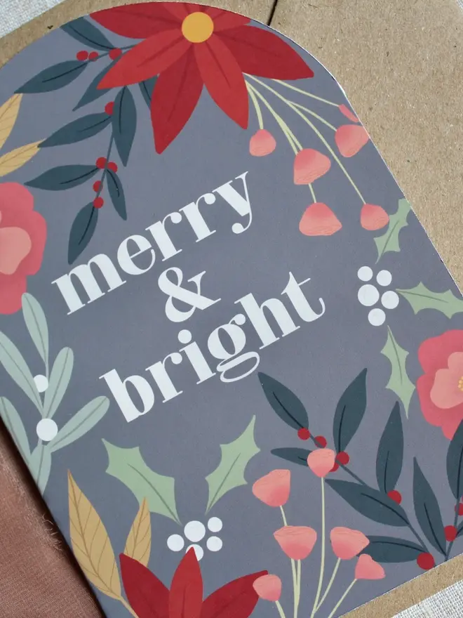 merry and bright floral christmas card. arch shaped card illustrated with flowers and emblazoned with merry christmas.