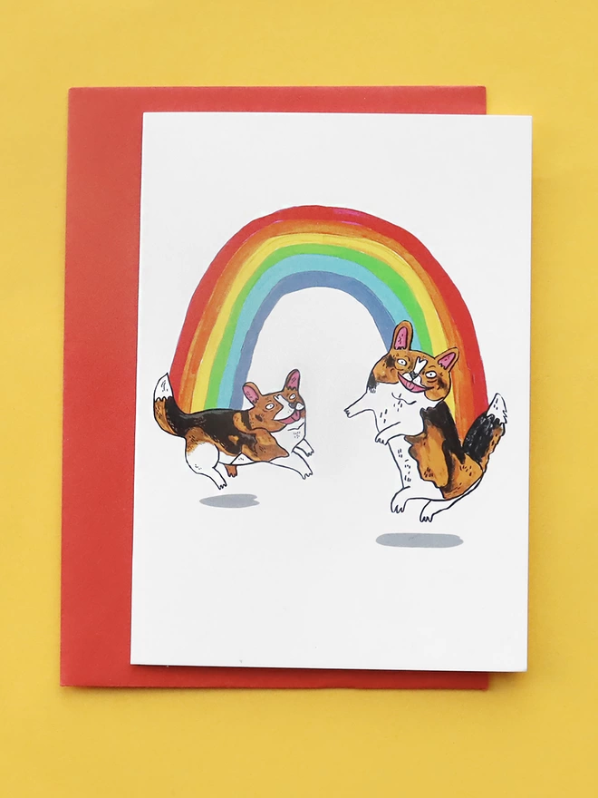 Illustrated rainbow with two dancing corgi's on each end of the rainbow on an A6 Greeting card