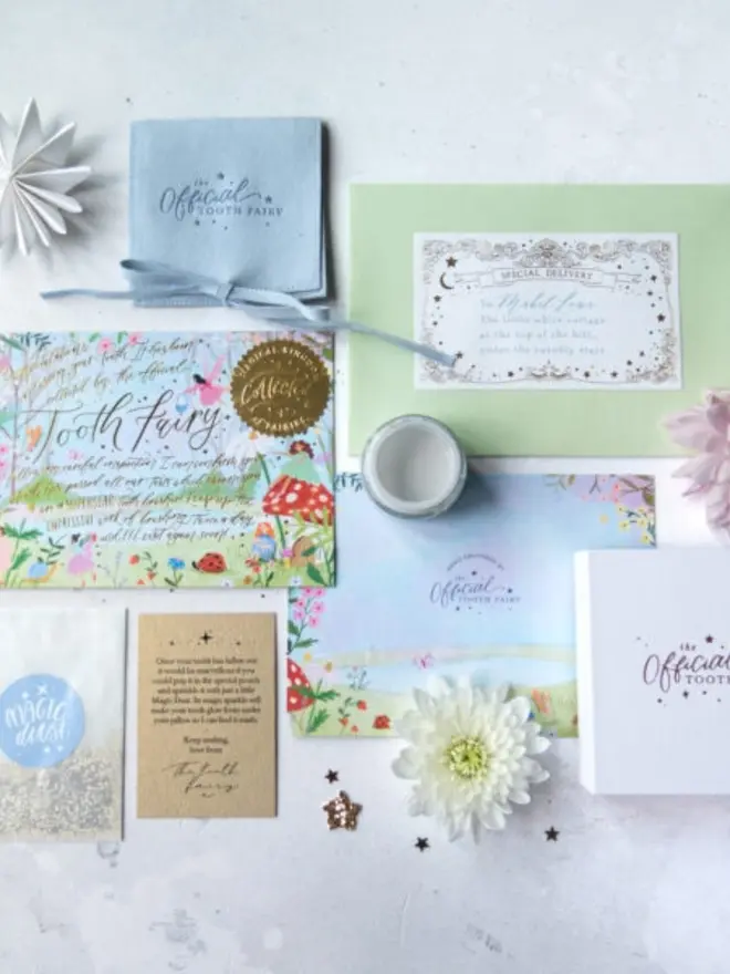 The full set from above: notecard, blue suede pouch, addressed envelope, Magic Dust and a note from the Tooth Fairy. A white gift box and a flower-illustrated backing card complete the layout.