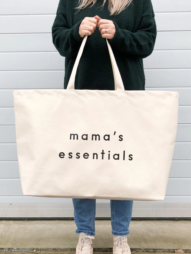 model holding a oversized natural canvas tote bag with mama's essentials slogan