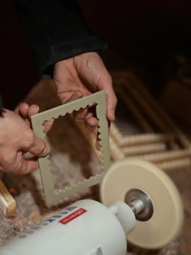 person sanding the edges of a pistachio stamp shaped frame mount