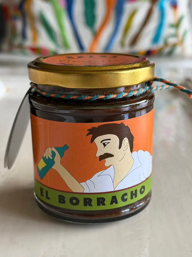 'El Borracho' Salsa Jar (Set Of 1-4 Jars), a salsa jar sitting on a white kitchen counter. It has an image of a man with a Mexican chilli. 