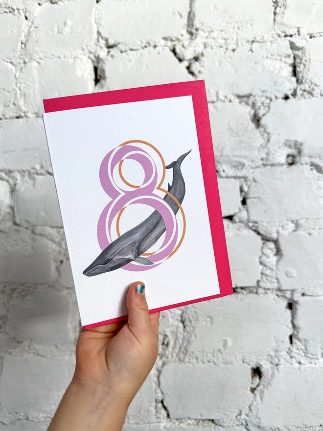 white card with a big pink number 8 and an illustration of a fin whale with a neon pink envelope