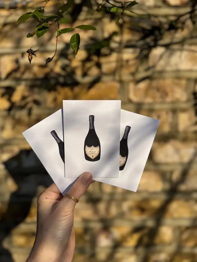 champagne bottle illustrated mini card (pack of 3). card set photographed against brick wall backdrop.