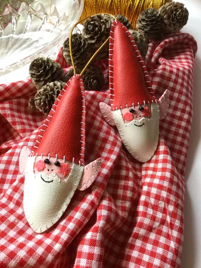 A hand stitched faux leather Christmas elf tree decoration, alongside a brooch version, on red gingham fabric background