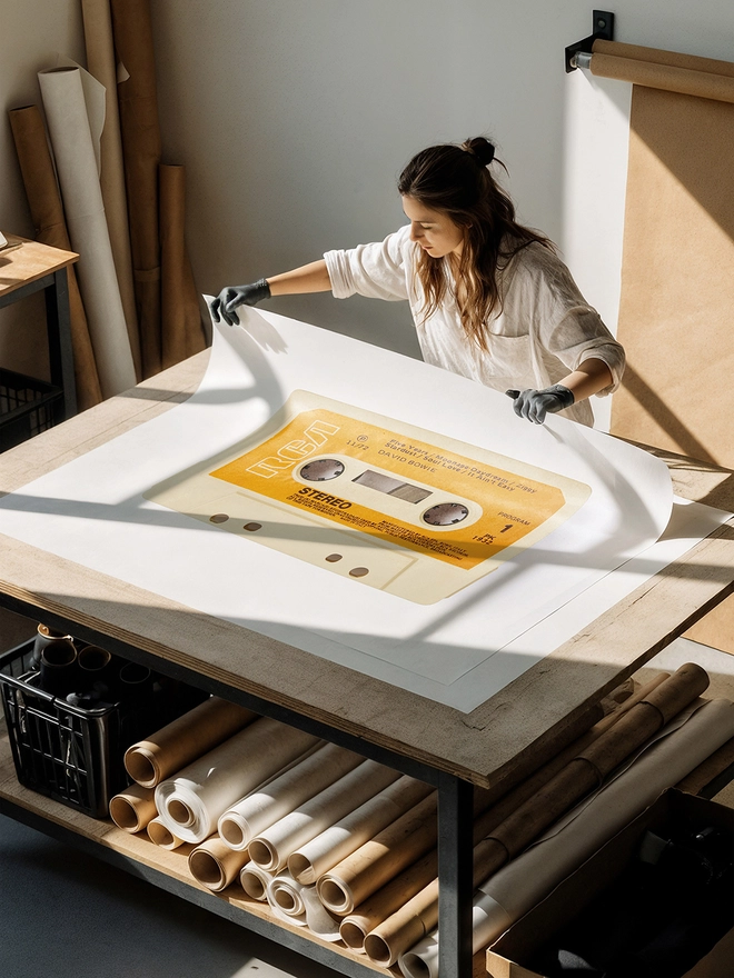 david bowie rise and fall of ziggy stardust cassette print. artist unrolling print on studio desk.