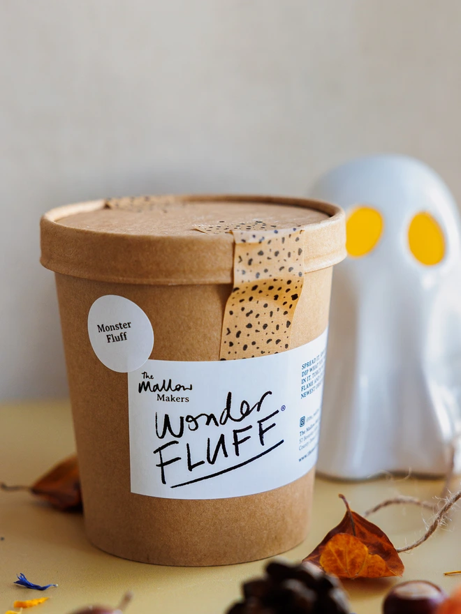 The Mallow Makers sealed tub of Monster marshmallow fluff beside a ghost with orange eyes