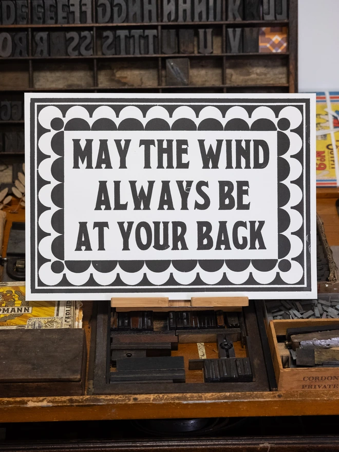 A3 letterpress print with vintage serif block font text design "may the wind always be at your back" surrounded by vintage art-deco style border made of semicircles and semi-circular cut-outs