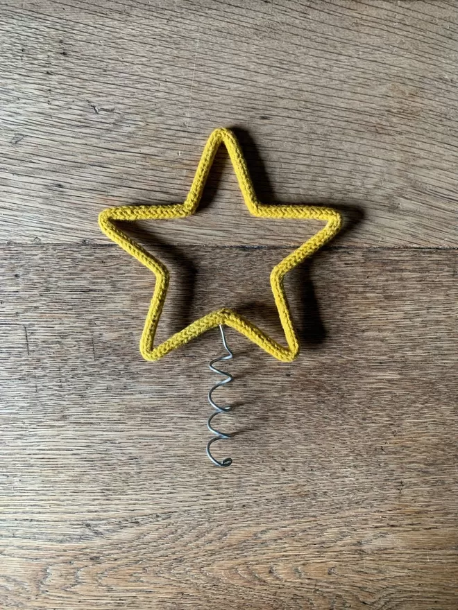 A small gold string wrapped wire star Christmas tree topper with a narrow coil on an oak table