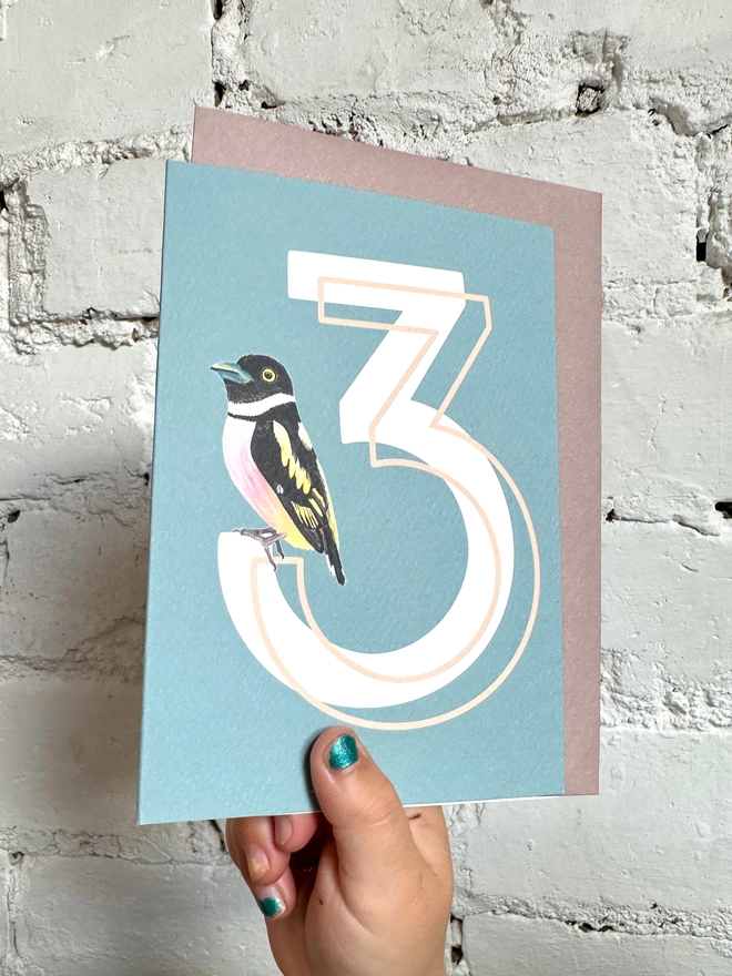 a blue card with a big white number 3 and an illustrated broadbill bird with a purple envelope