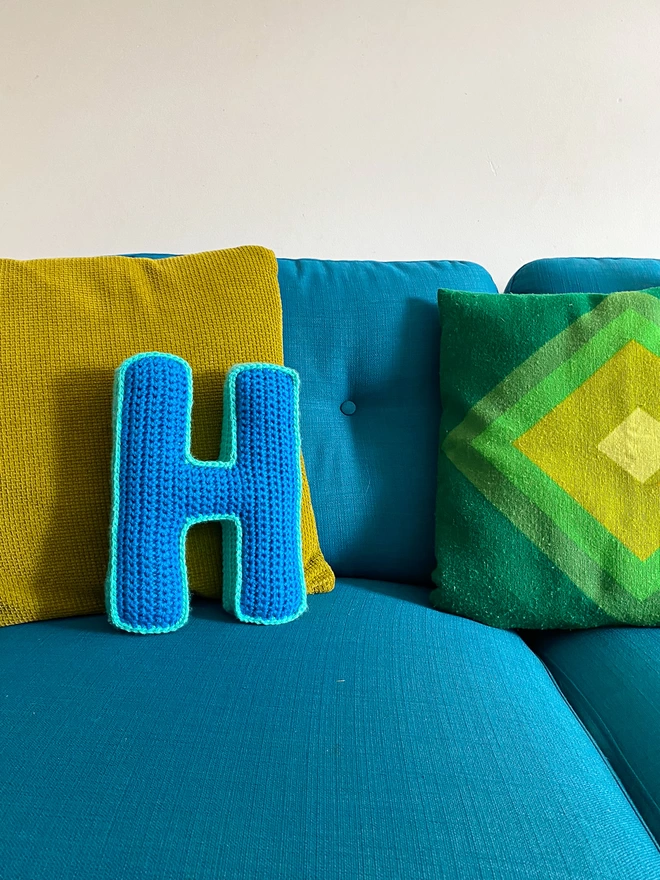 Crochet Cushion shaped like an H in Light Blue & Teal on a turquoise sofa