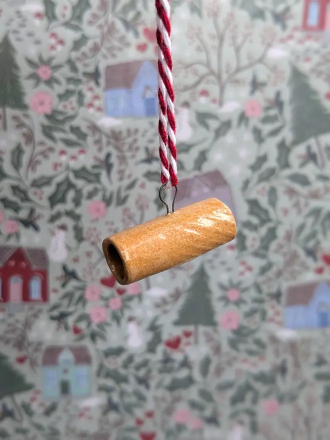 ceramic rigatoni christmas decoration. a small pasta ornament hanging from red and white thread.