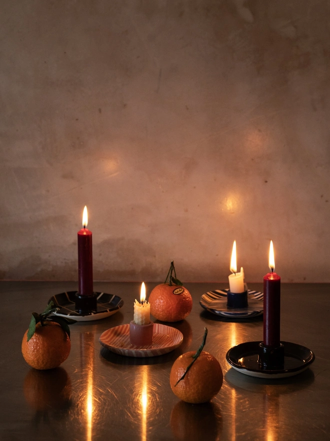 Ceramic Patterned Candlestick Holder, a group of colourful candlestick holders sitting on a dark floor. They are accompanied by lit candles. 