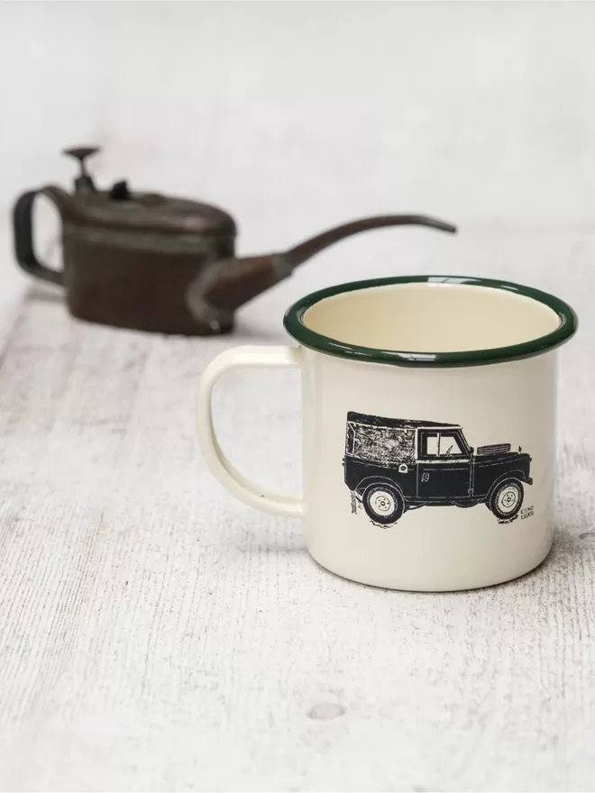 Picture of a Cream Enamel Mug with a Green Rim with a Land Rover design etched onto it, taken from an original Lino Print