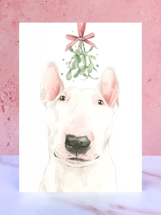 A Christmas card featuring a hand painted design of a English Bull Terrier, stood upright on a marble surface.