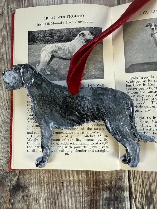 Irish Wolfhound Handpainted wooden Christmas Decoration placed on a book about dogs and hung with red velvet ribbon