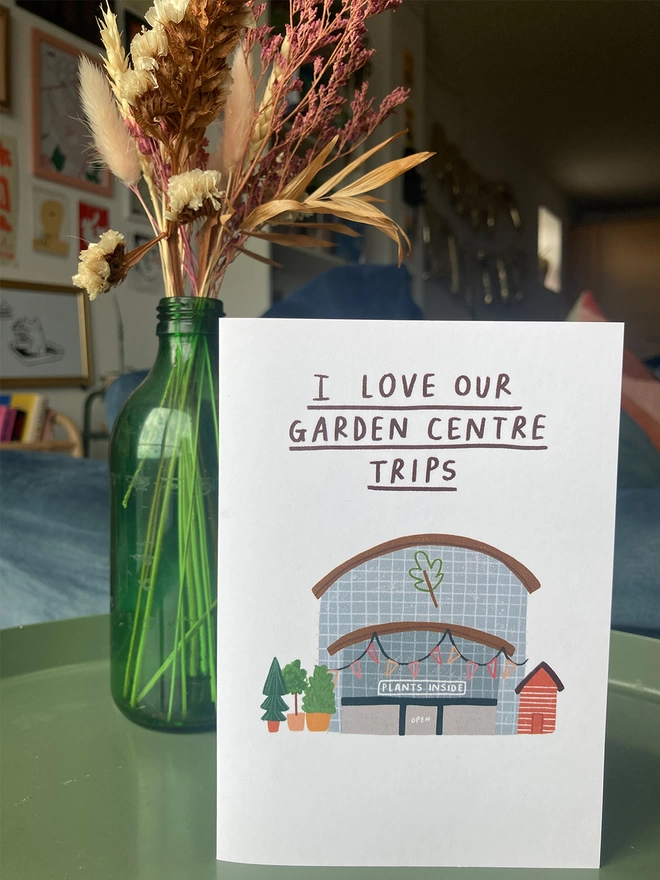 Greetings card with message 'I love our garden centre trips', placed on a table with flowers in the background.