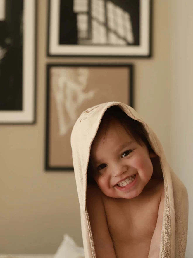 A baby wearing all smiling wearing the hooded towel