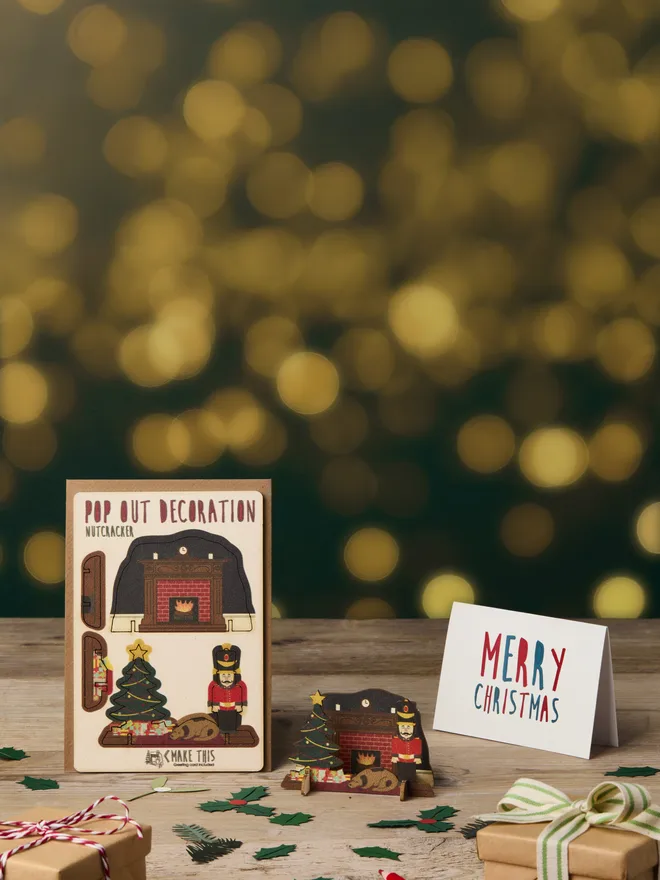 Pop out laser-cut nutcracker Christmas decoration and Merry Christmas card and brown kraft envelope on top of a wooden desk in front of a festive lights background
