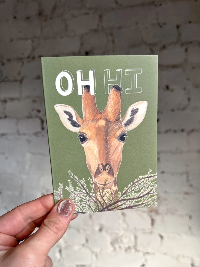  a green greetings card featuring an illustration of a giraffe peering over a bush