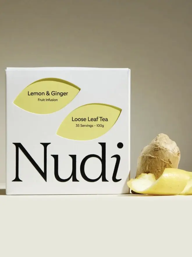 white box of ginger lemon tea with yellow design next to piece of ginger and lemon peel
