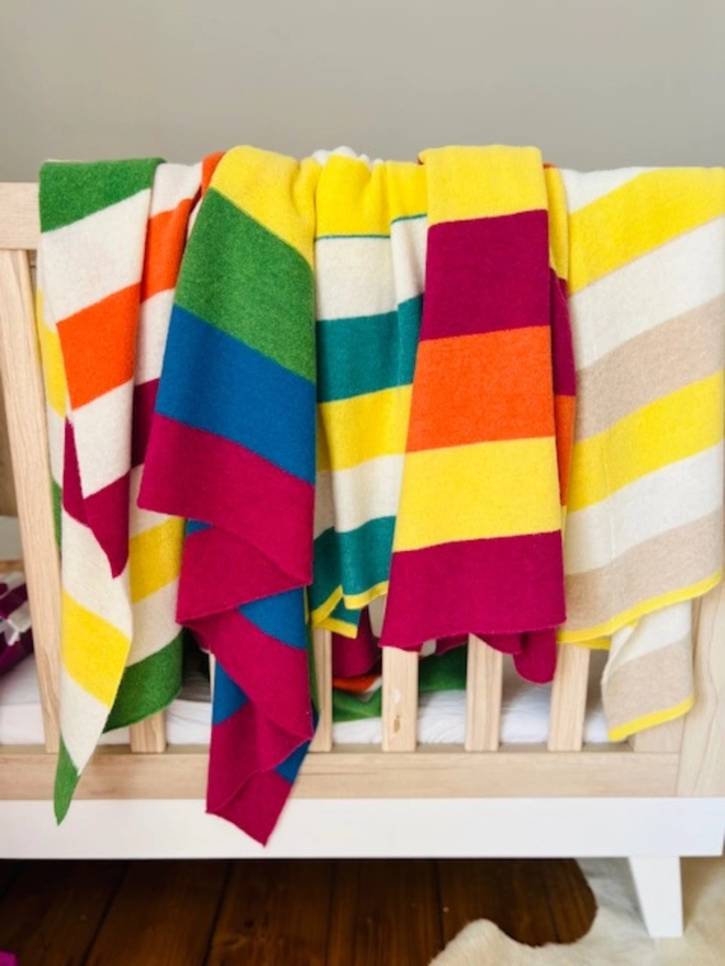 Collection of knitted striped blankets draped over the edge of a babies cot