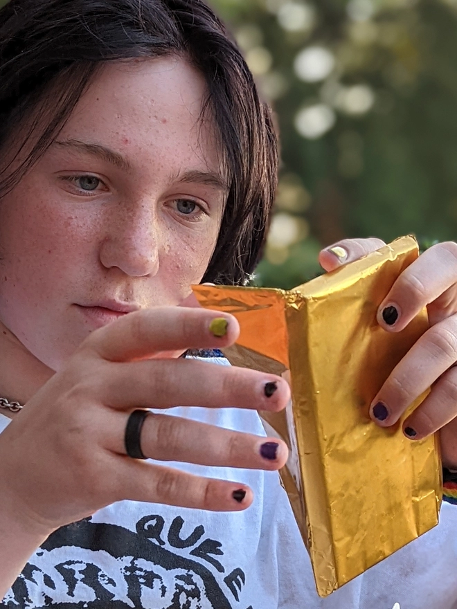 Happy young teenager opening gold foil wrapped charity dark chocolate with honeycomb bar