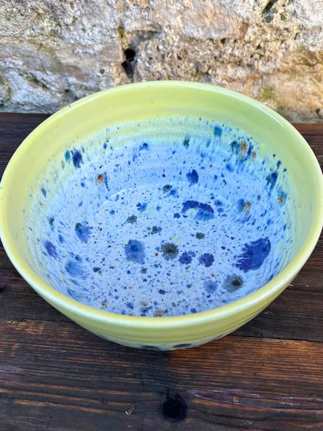 Shoreline Small Bowl, a colourful bowl placed on a wooden surface in front of a brick wall. 