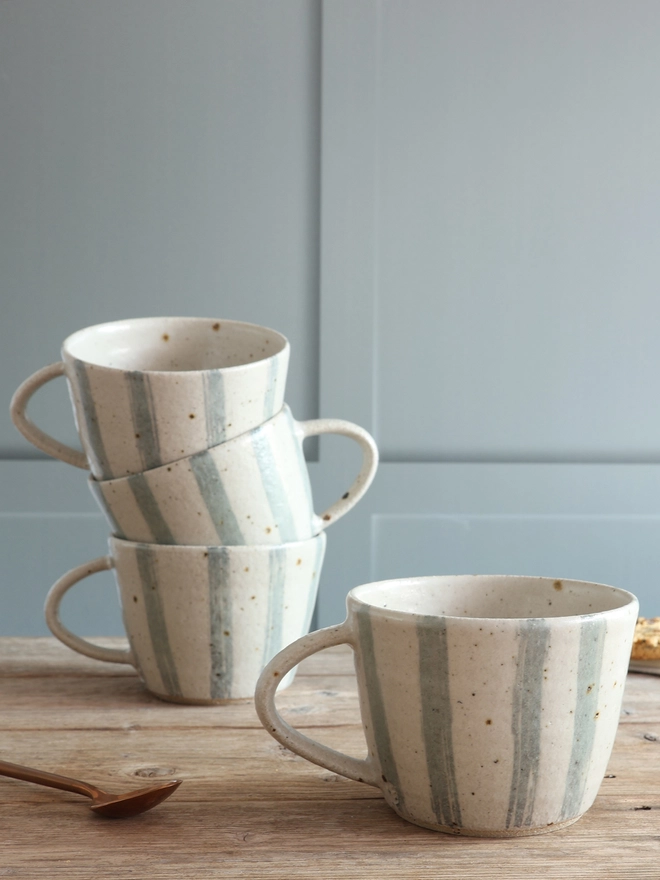 Handmade Ceramic Stoneware Mug in Blue and White Stripe sat on a wooden surface. The background shows three of these mugs stacked on top of each other.