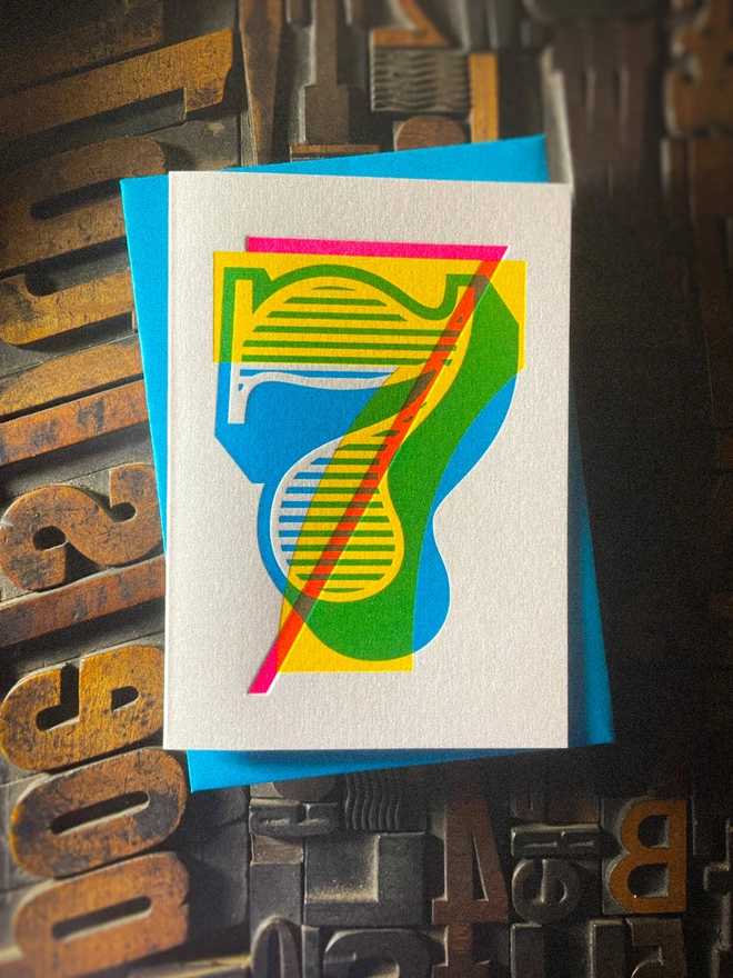 Handmade letterpress 7th birthday card featuring bold overlapping numerals printed in vibrant fluorescent cyan, magenta and yellow inks. Each card is individually hand printed using traditional letterpress techniques on luxury paper stock, creating a beautifully tactile finish with a deep impression and rich layered colours inspired by the CMYK printing process. Printed on a traditional letterpress from 1915. A wonderful artisan printed birthday card.