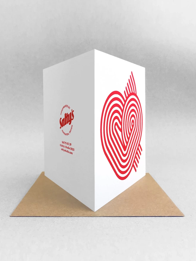  A rear view of the stripy heart card, comprising six magenta swirling stripes creating a neat heart-like graphic on the front. Card is stood on a kraft brown envelope in a studio with light grey background.