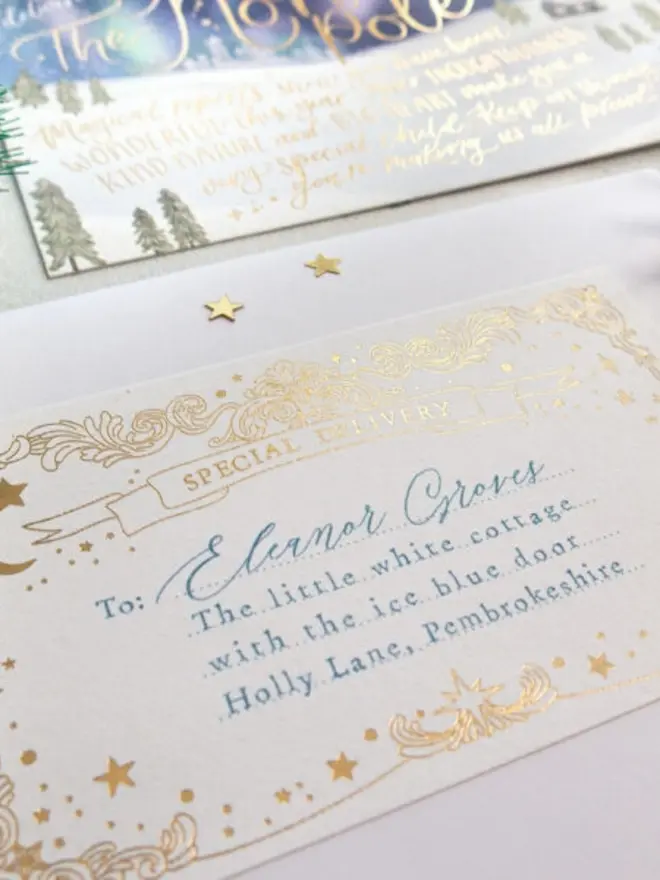 A close-up of a personalised gold foil "Special Delivery" label with stars and a crescent moon, addressed in blue "To: Eleanor Groves, The little white cottage with the ice blue door, Holly Lane, Pembrokeshire".