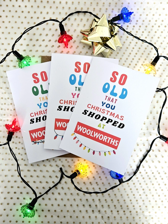 An image of three colourful Christmas cards that say so old you Christmas shopped at Woolworths with Christmas lights and baubles round them