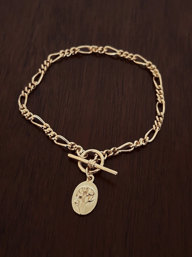 Gold plated forget me not charm with a figaro t bar bracelet