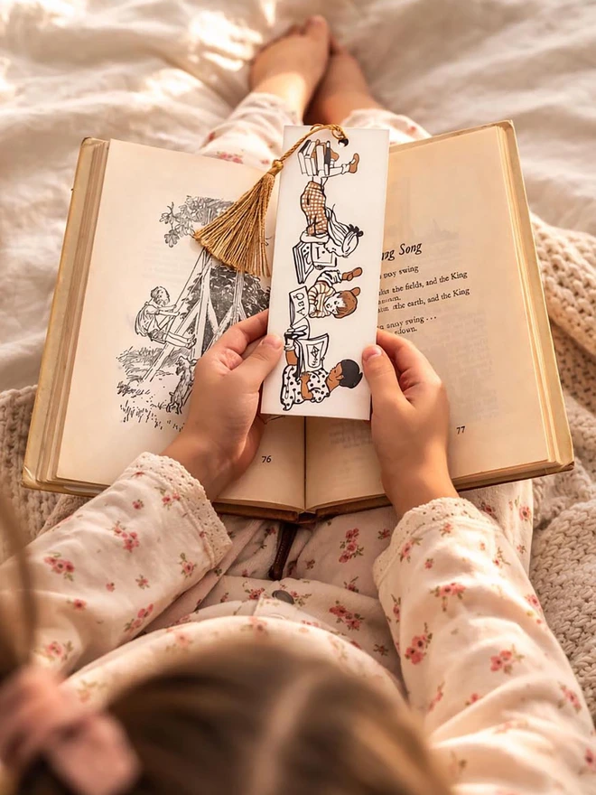a photograph of a little girl holding a traditional illustrated bookmark featuring illustrations of children reading their story books a traditional cardboard bookmark complete with silky tassel