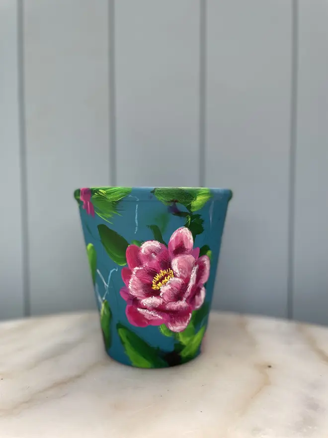 Unique hand-painted terracotta pot featuring pink peony on a turquoise background