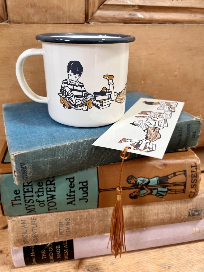 a cream enamel mug screen printed with children reading books cream in colour with a grey rim sat on a pile of vintage books