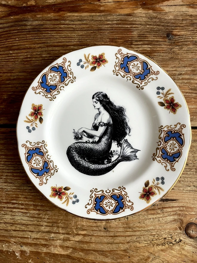 vintage plate with an ornate border, with a printed vintage illustration of mermaid in the middle