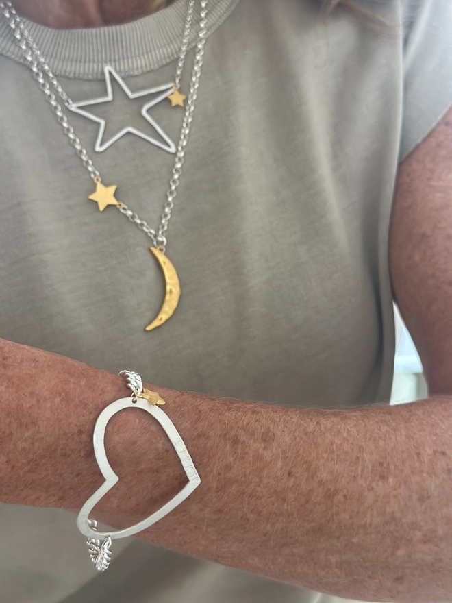 model wears a personalised large open heart charm in silver on chunky curb chain with a small gold star charm. 
