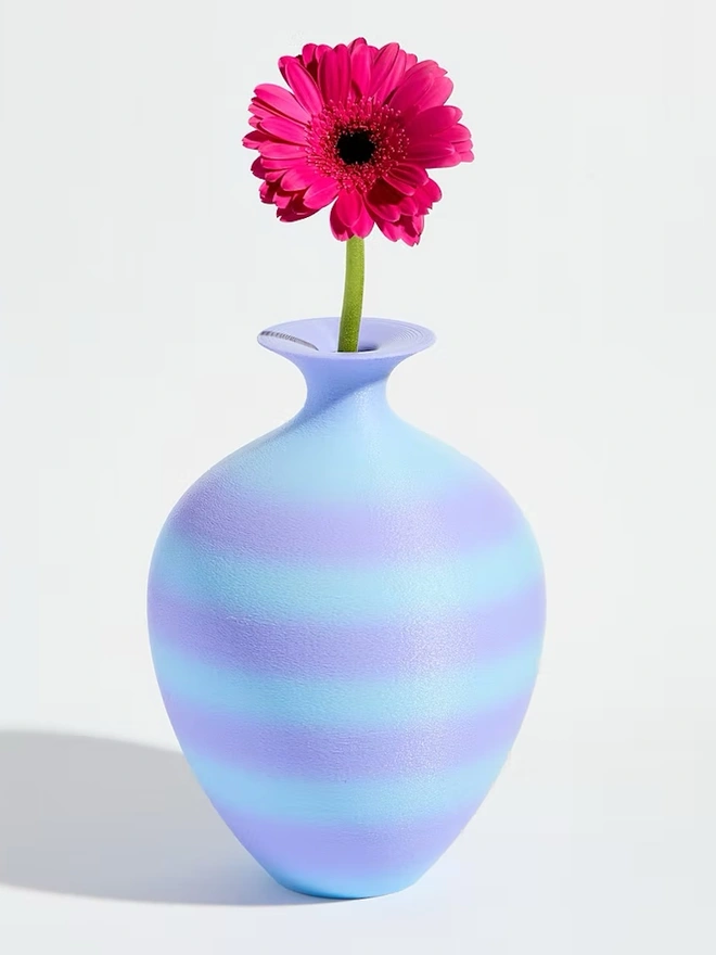 3d printed vase in blue and purple stripes with bright pink flower