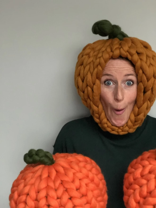 Two knitted pumpkins held up by the maker wearing a halloween pumpkin.