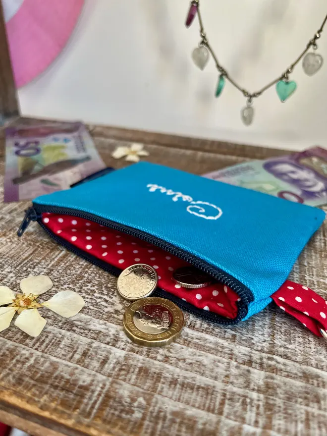 Small blue zip coin pouch with red polka dot lining with coins spilling out of the open zip.