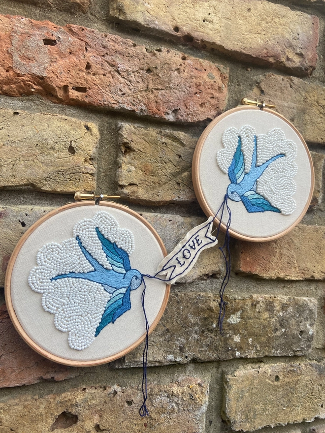 Two embroidery hoops with blue swallows holding a banner